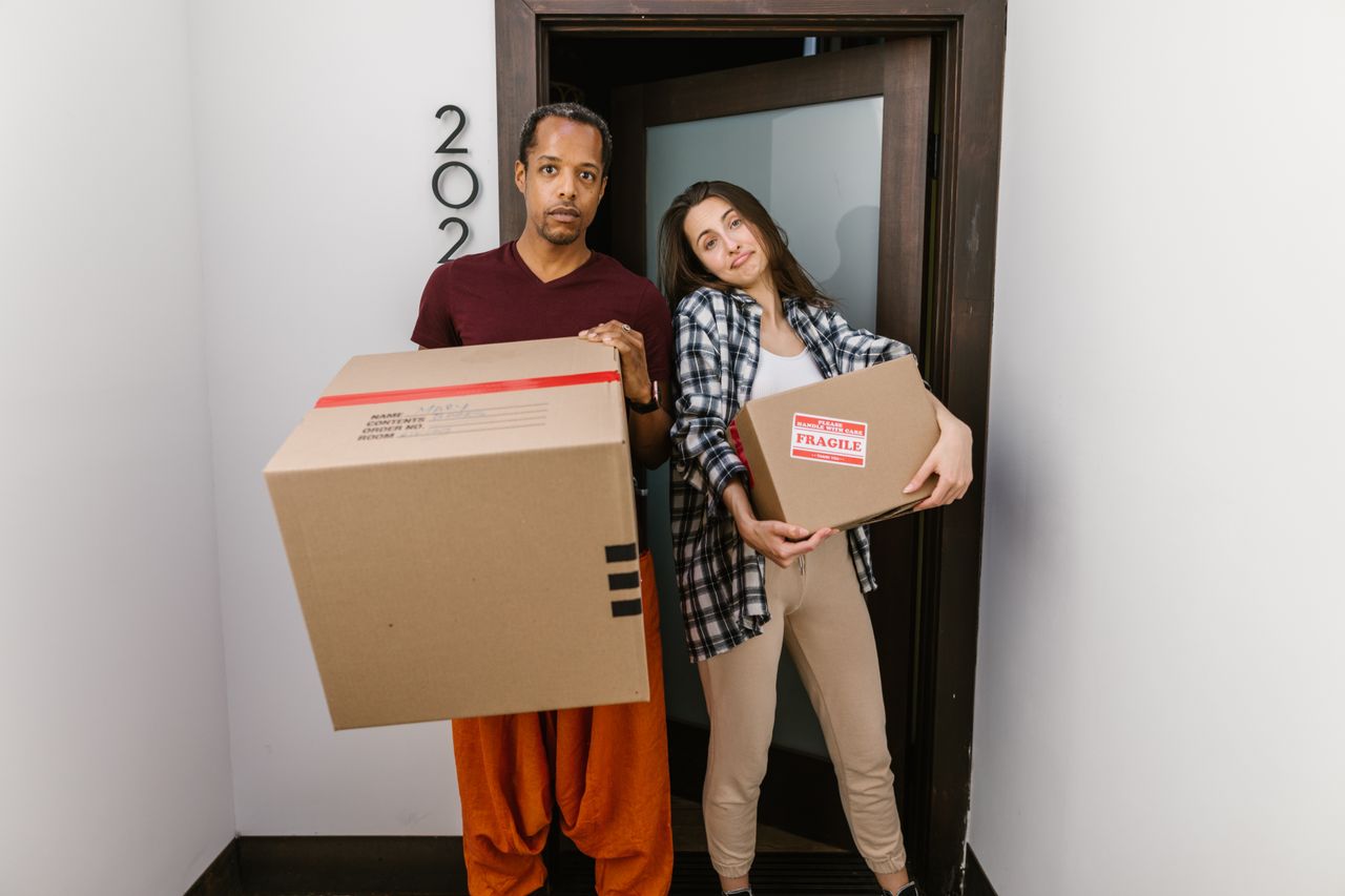 services-04 A couple carrying moving boxes indoors, settling into their new apartment.